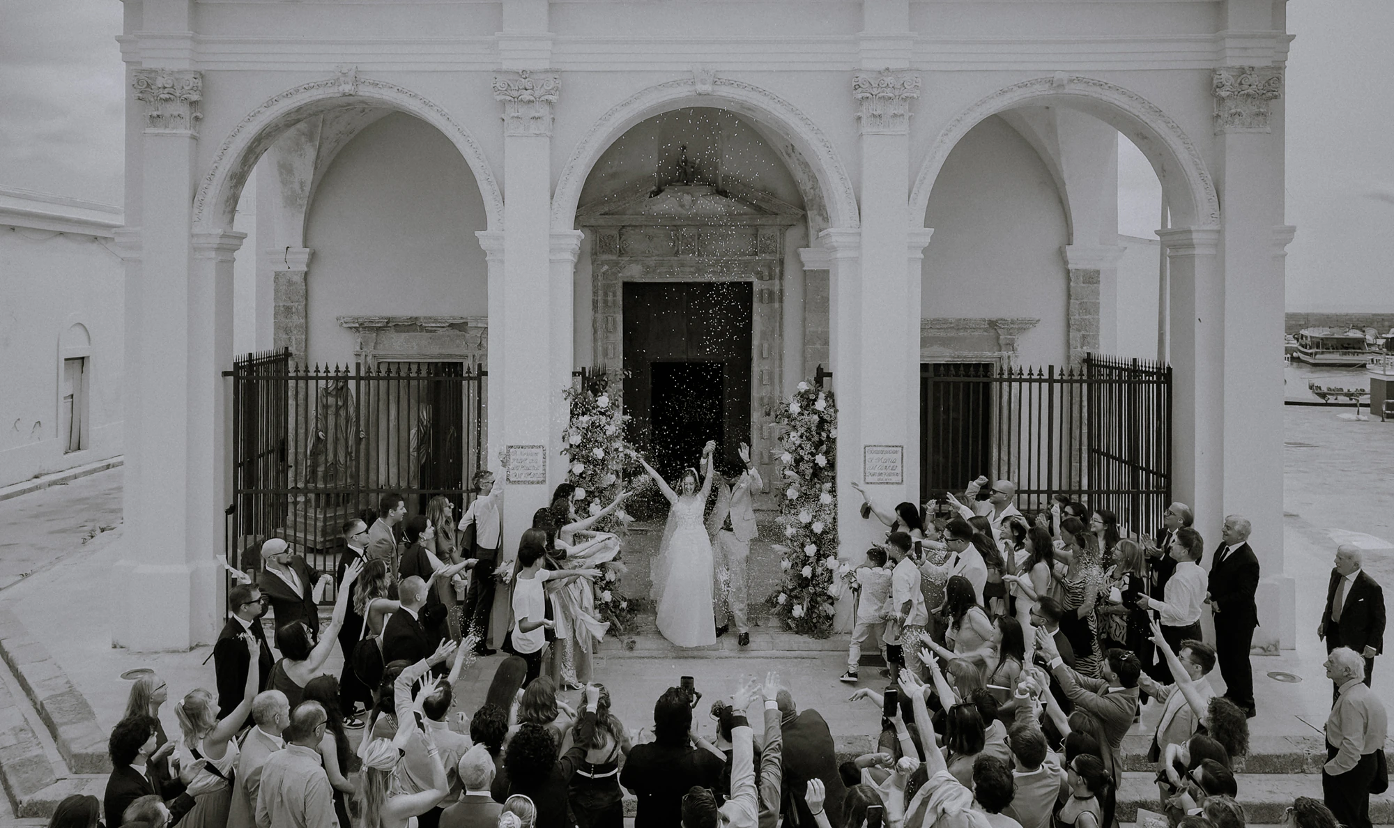 Gli invitati festeggiano gli sposi sulla porta della chiesa, in bianco e nero