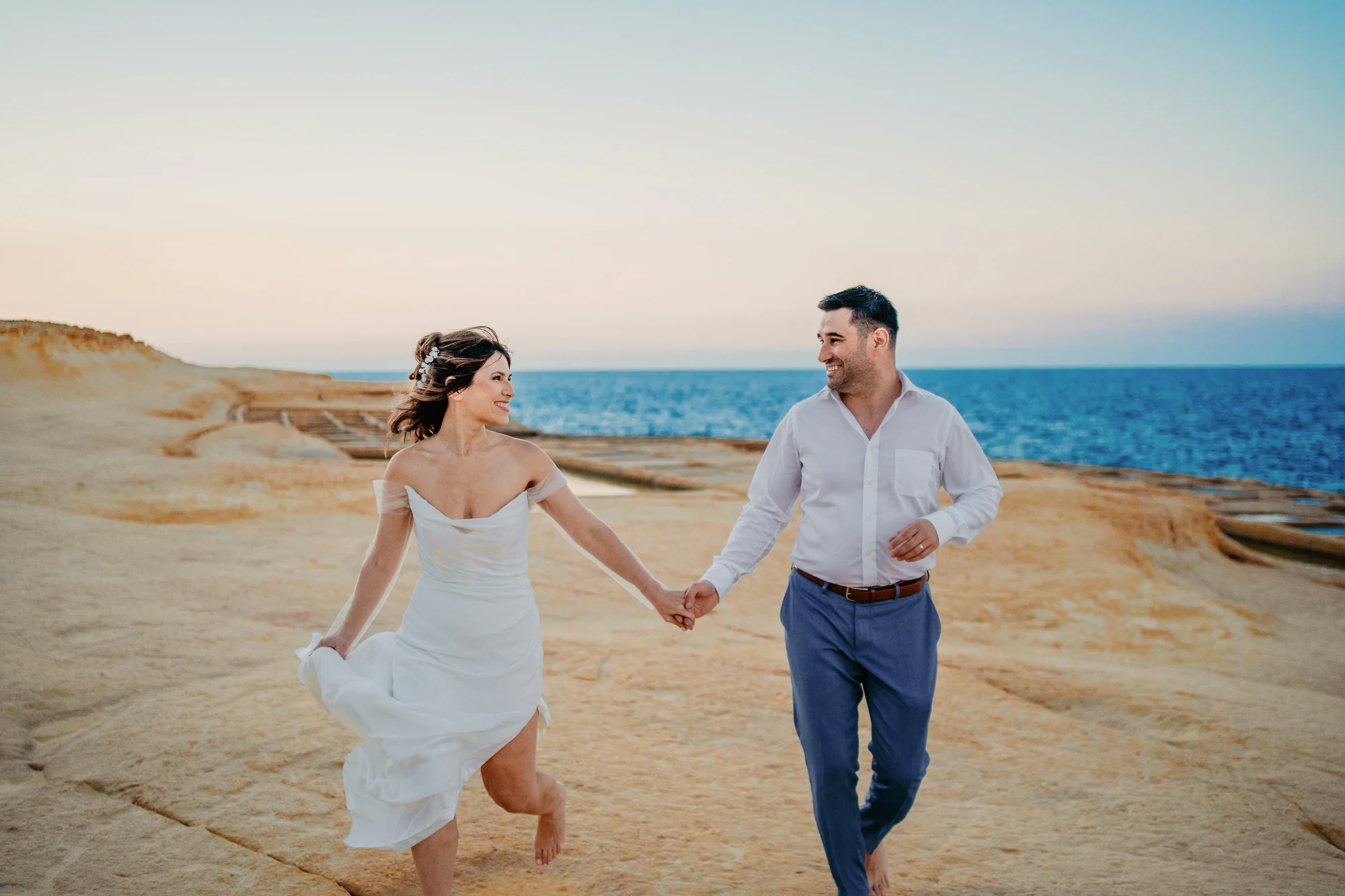 Gli sposi corrono mano nella mano sulla costa di Malta
