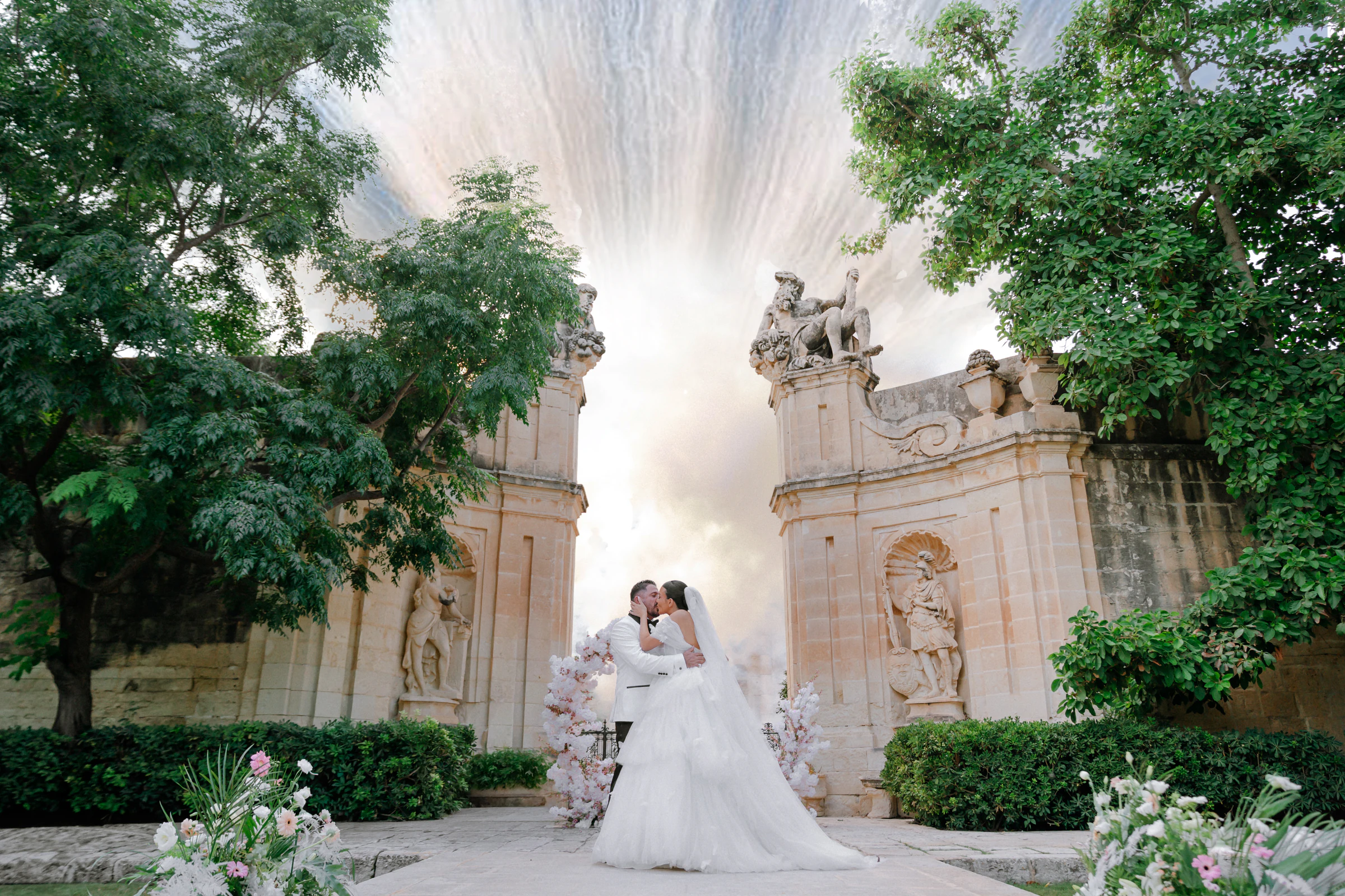 Bacio degli sposi tra le colonne in pietra di una villa, avvolti dal fumo bianco della smoke bomb