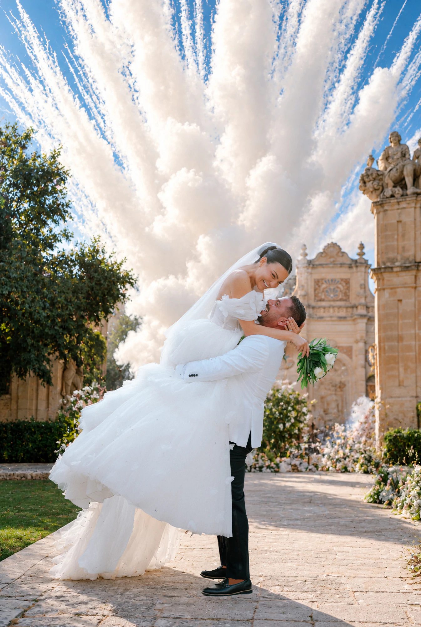 Lo sposo solleva la sposa sotto una smoke bomb bianca con il cielo azzurro